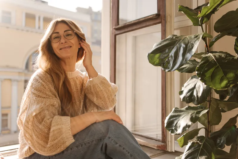 Mujer sentada junto a una ventana, con una taza entre las manos, en un momento de calma